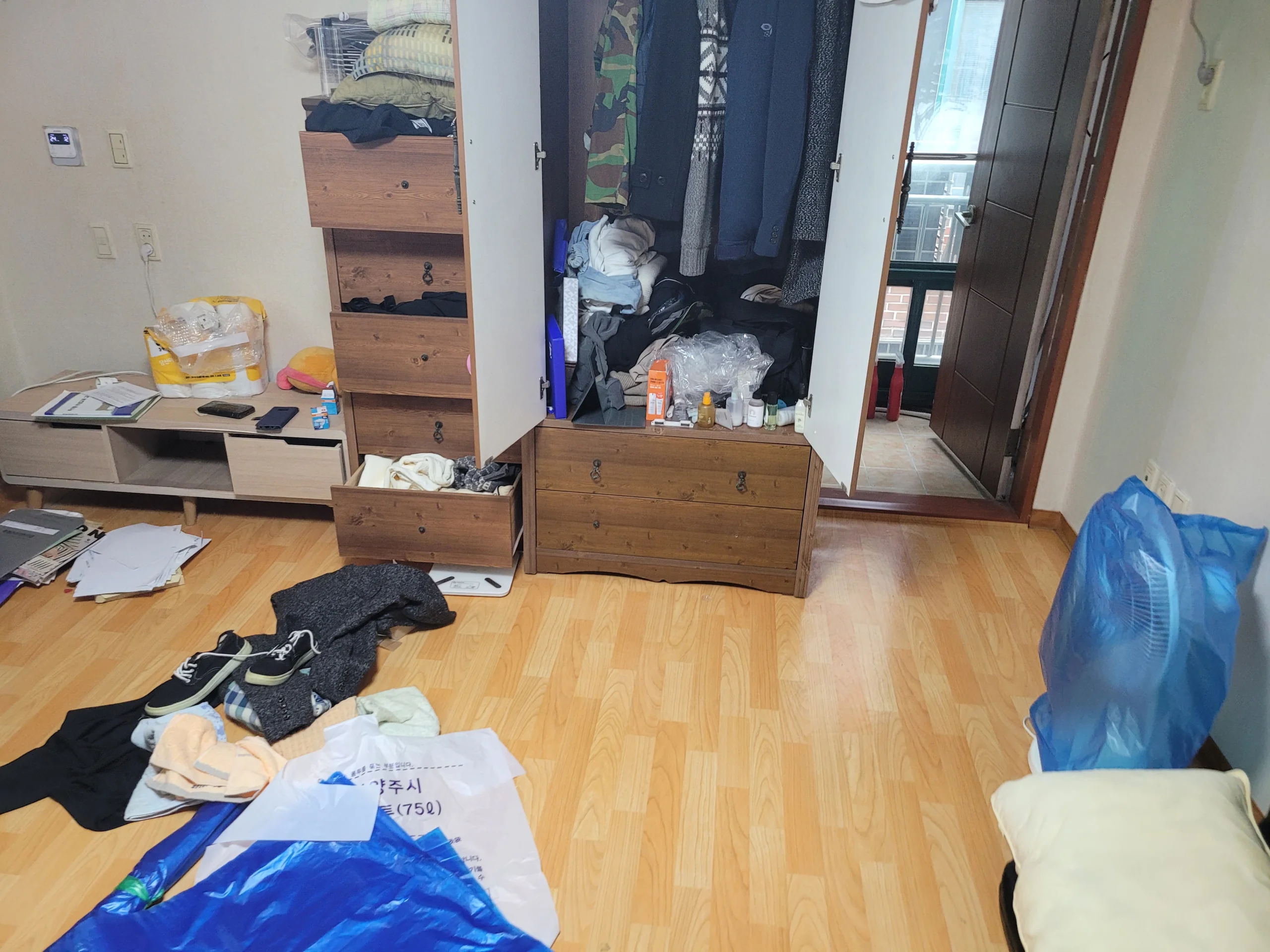 빌라 방 안 서랍장 앞에 종량제 봉투와 옷가지가 놓여 있는 모습
