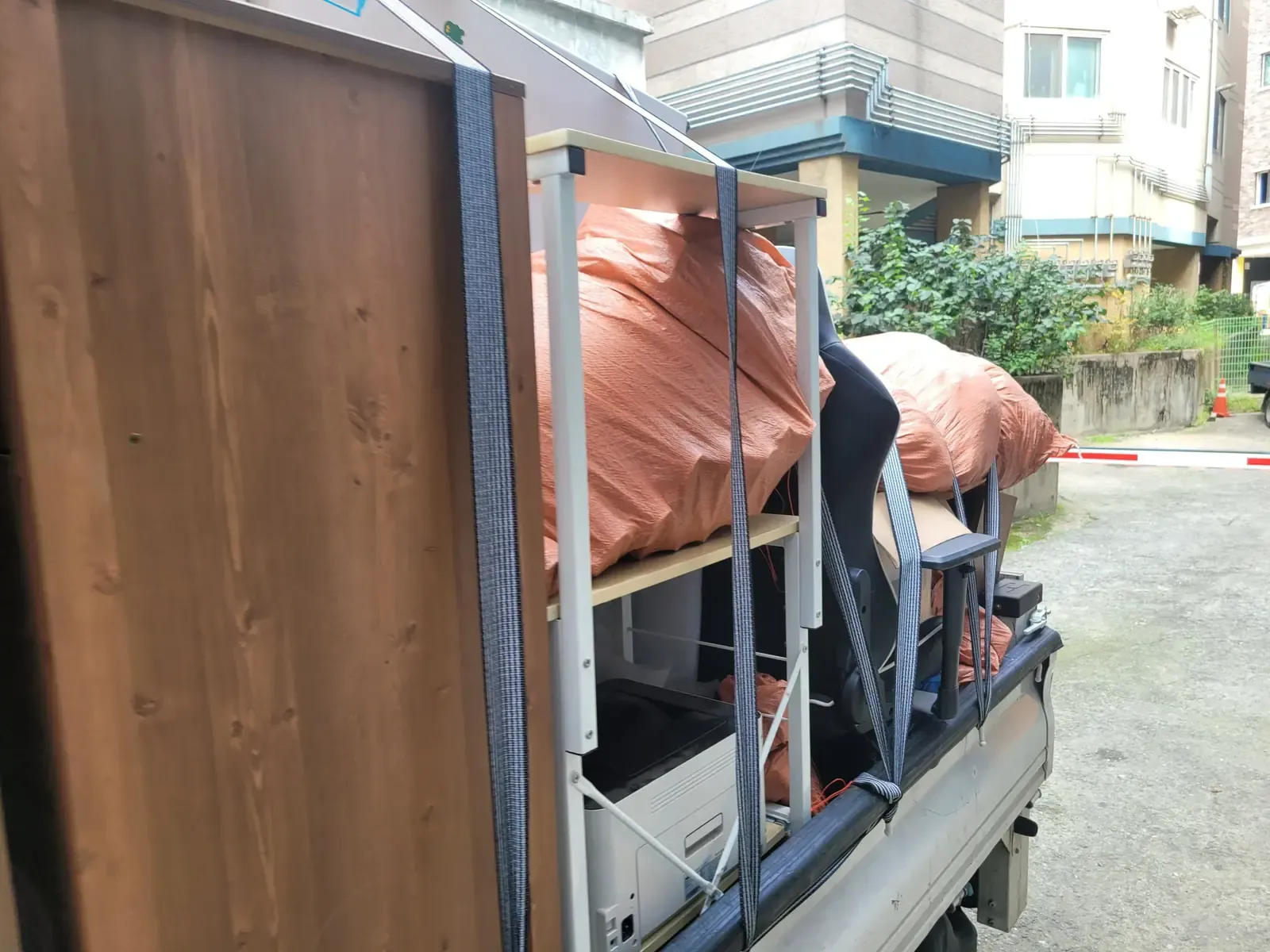 좁은 주차장에서 트럭에 큰 목재 패널과 마대를 싣고 있는 모습